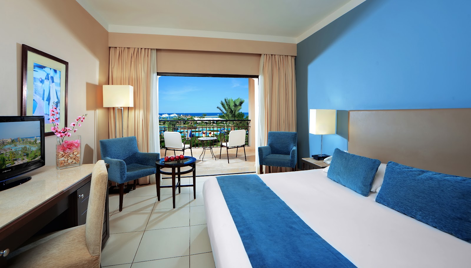 Resort suite with bed, seating area, and balcony overlooking beach and pool at Jaz Aquamarine Resort.