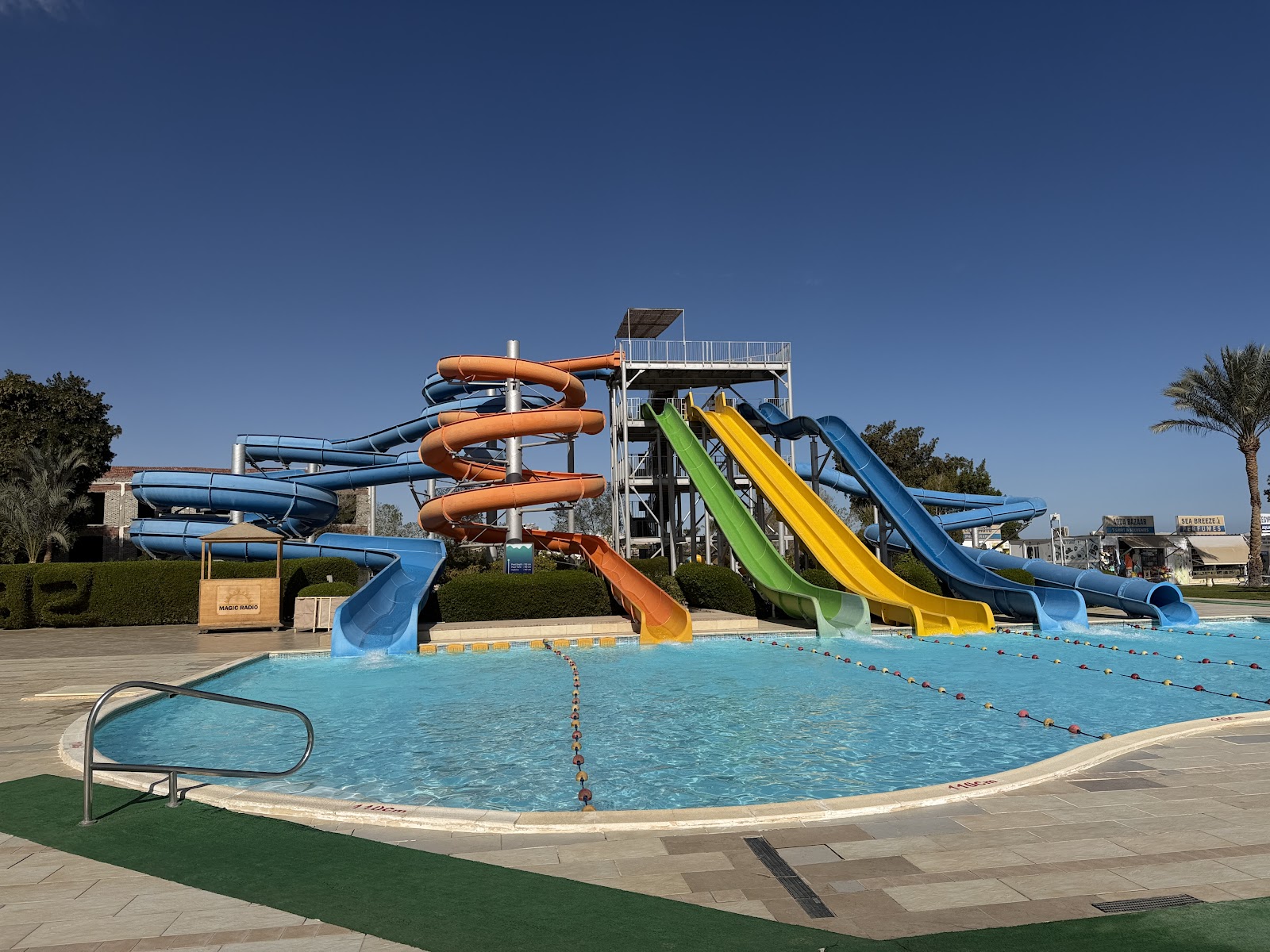 Water slides in blue, orange, and yellow spiral over a resort pool with lane dividers under clear sky.