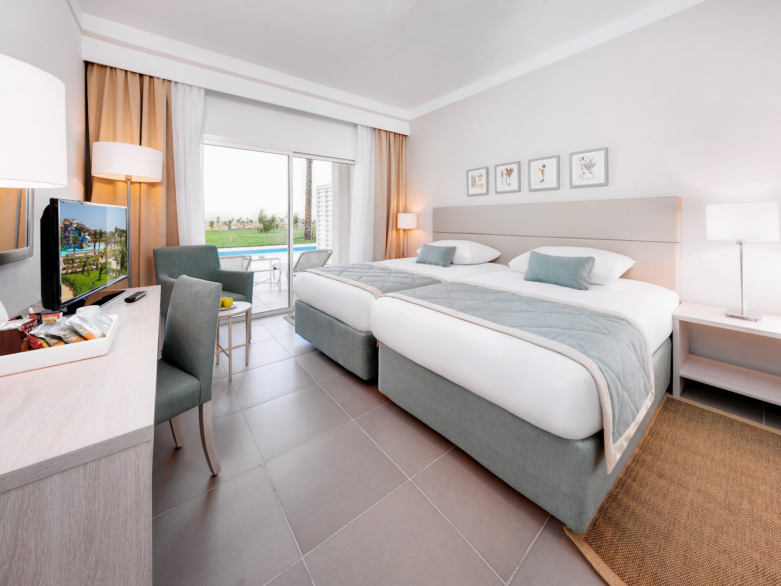 Hotel room with two twin beds, sitting area, and balcony overlooking green grounds at JAZ Aquaviva.