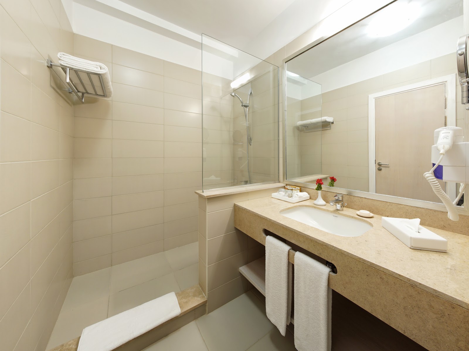 Modern bathroom with beige tile walls, glass-enclosed shower, stone vanity with white sink, and white towels at JAZ Aquaviva resort.