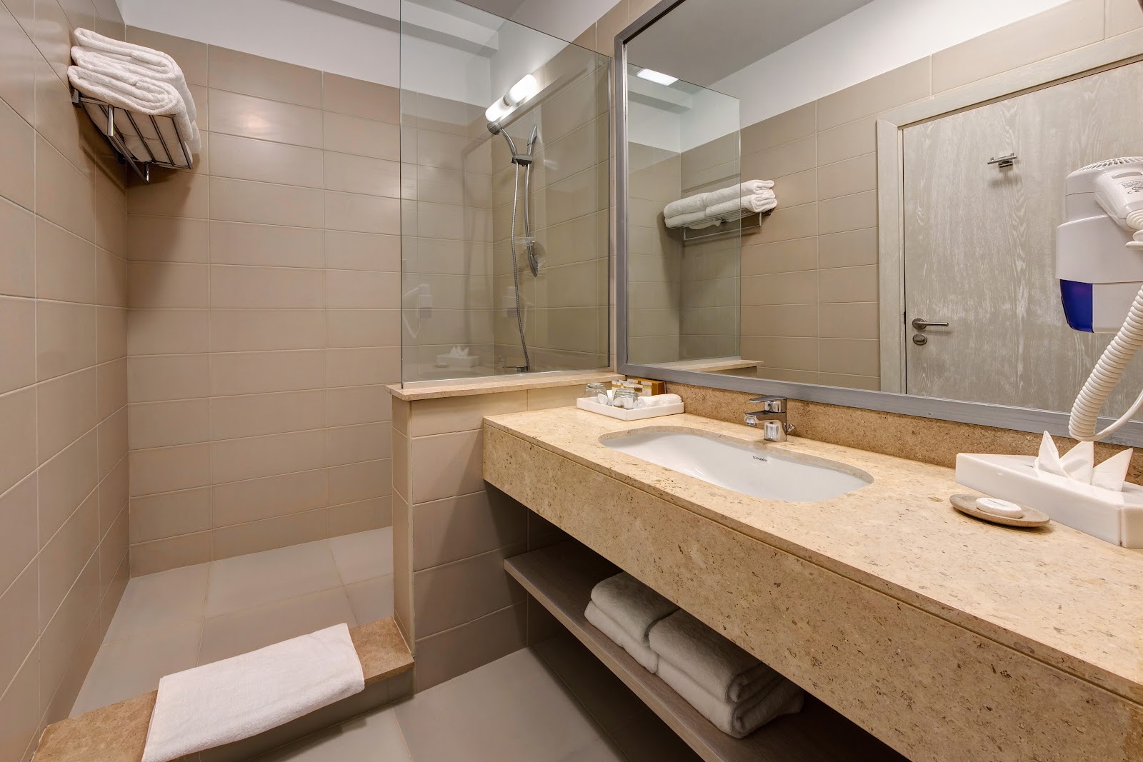 Modern bathroom with stone countertop sink, glass shower enclosure, and white towels at JAZ Aquaviva.