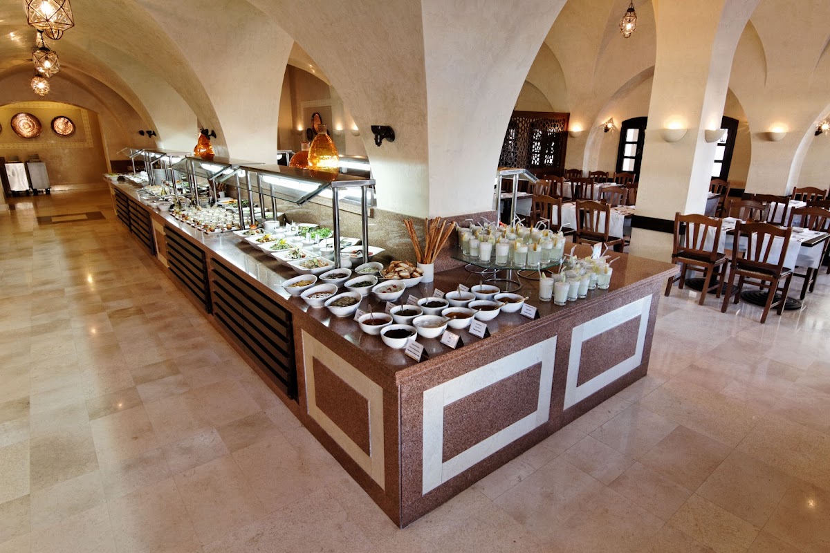 Dining room with vaulted archways displaying buffet stations of appetizers and sauces, wooden chairs, and pendant lighting.