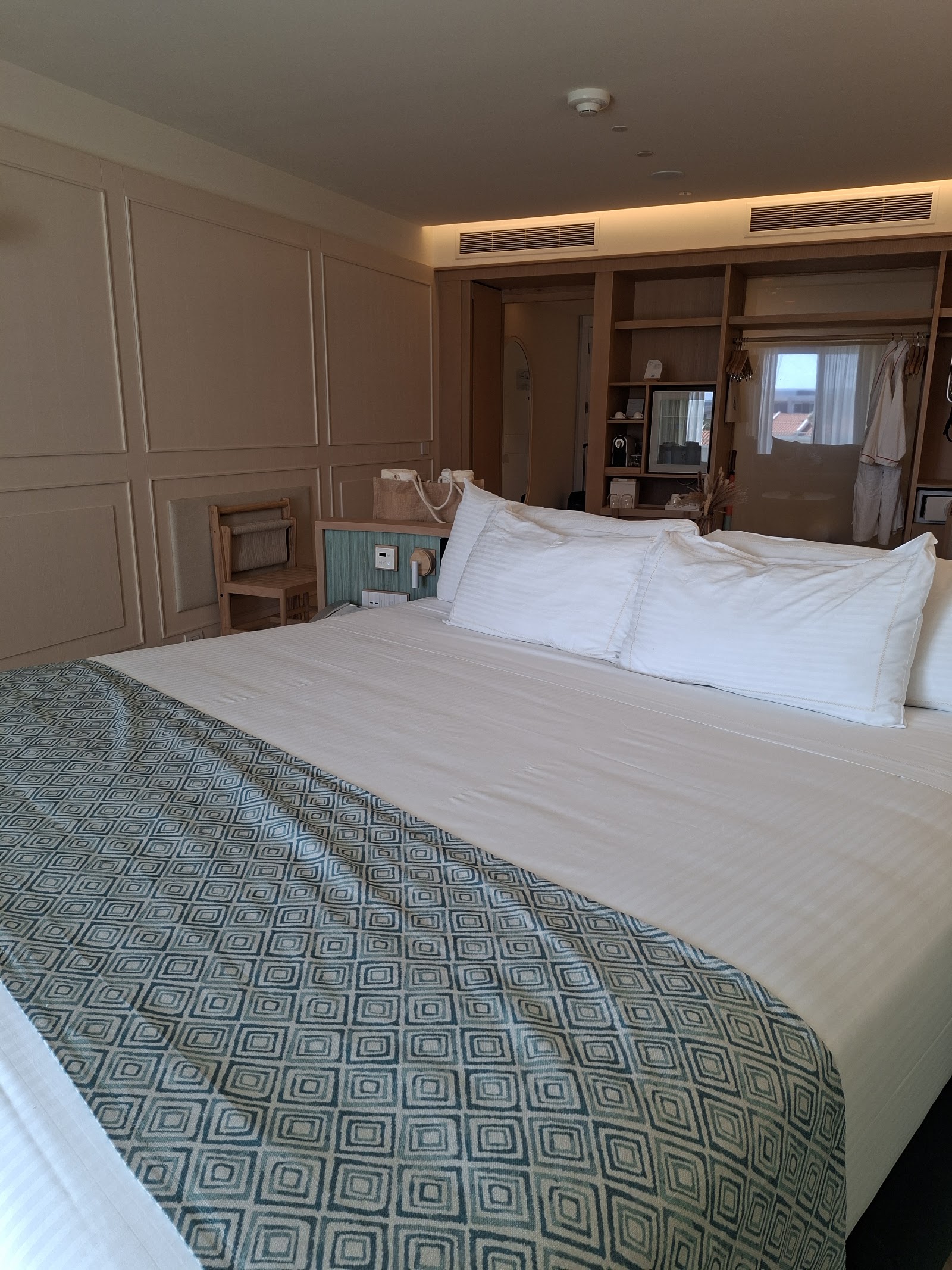 Resort bedroom with two queen beds, white pillows, geometric patterned bedding, paneled walls, and a walk-in closet visible in the background.