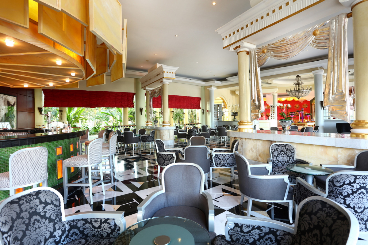 Elegant lobby lounge with patterned armchairs, marble floors, red window shades, and decorative columns at JOIA Paraíso by Iberostar.
