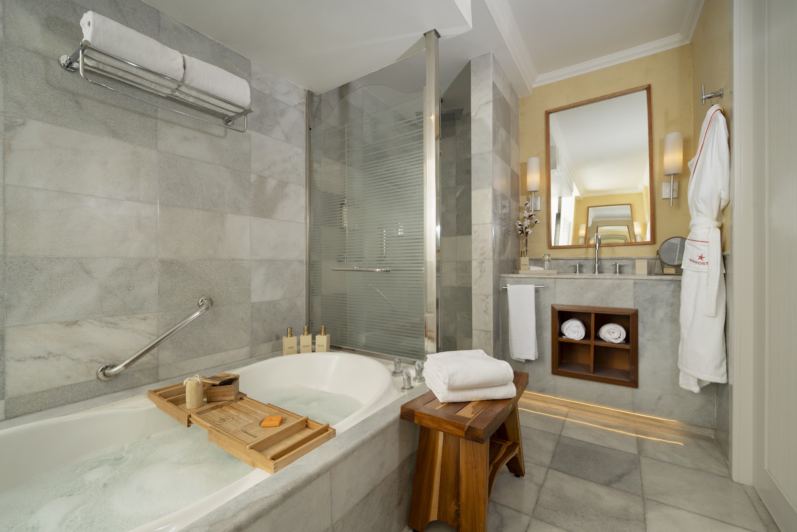 Modern bathroom with gray tile walls, soaking tub with wooden caddy, walk-in shower, and yellow-painted vanity area at JOIA Rose Hall by Iberostar.