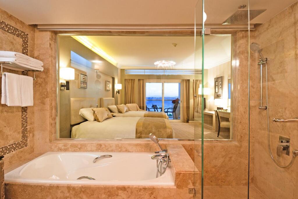 Marble bathroom with soaking tub and glass shower opening to bedroom with ocean view at KaiSol Romance Resort Sahl Hasheesh.