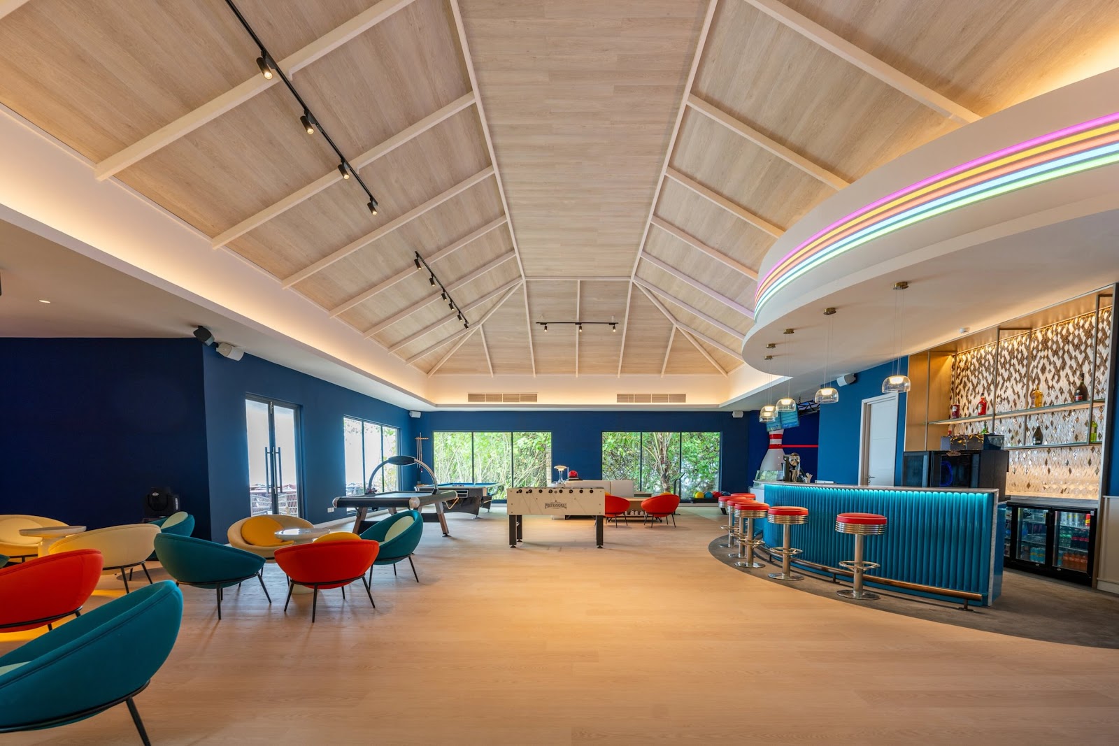 Modern resort restaurant with red and yellow chairs, geometric room dividers, warm lighting, and ocean views through floor-to-ceiling windows at dusk.