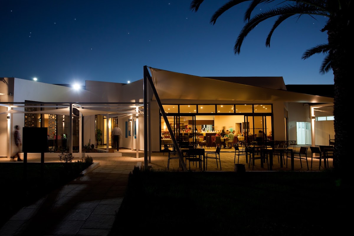 Evening view of TUI SUNEO Kenzi Europa's lit dining pavilion with guests seated at tables on the terrace under a starry sky.