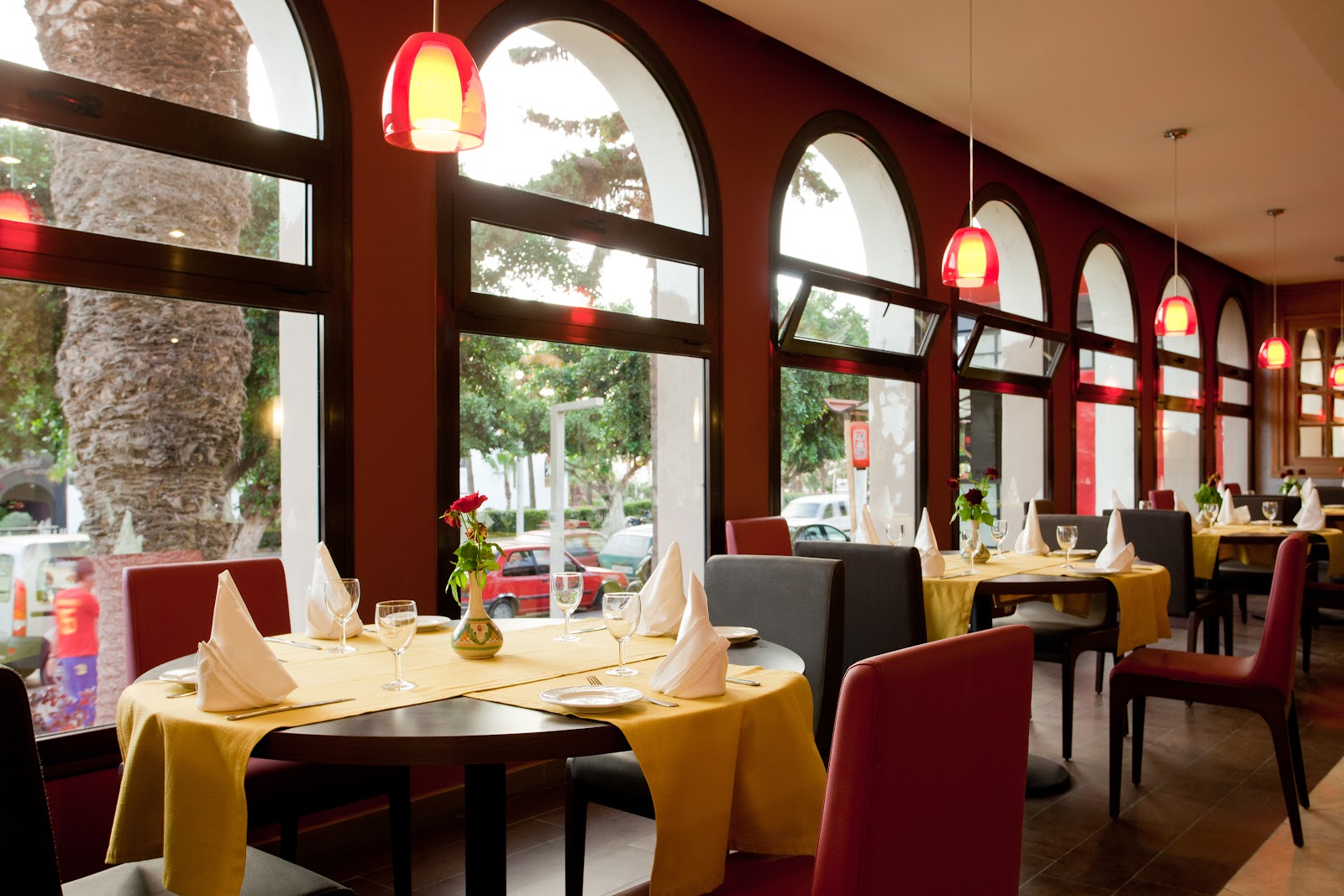 Fine dining restaurant with gold tablecloths, burgundy chairs, large arched windows with red pendant lights, and views of palm trees outside at TUI SUNEO Kenzi Europa.