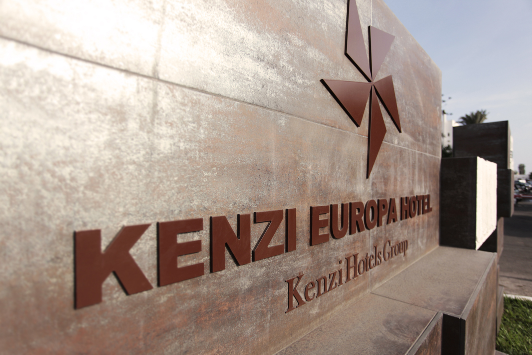 Kenzi Europa Hotel signage on a light stone wall with decorative copper stars and palm trees visible in the background.