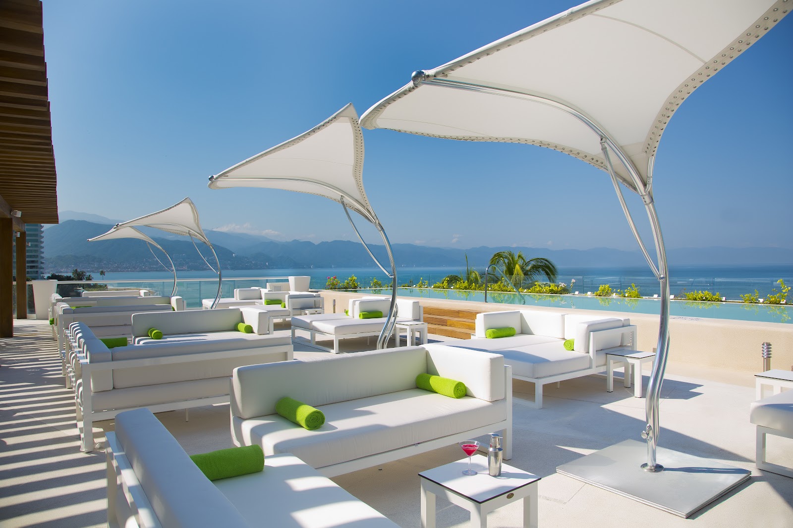 Beachfront dining terrace at Krystal Grand Puerto Vallarta with white umbrellas, set tables, and ocean view under clear blue sky.