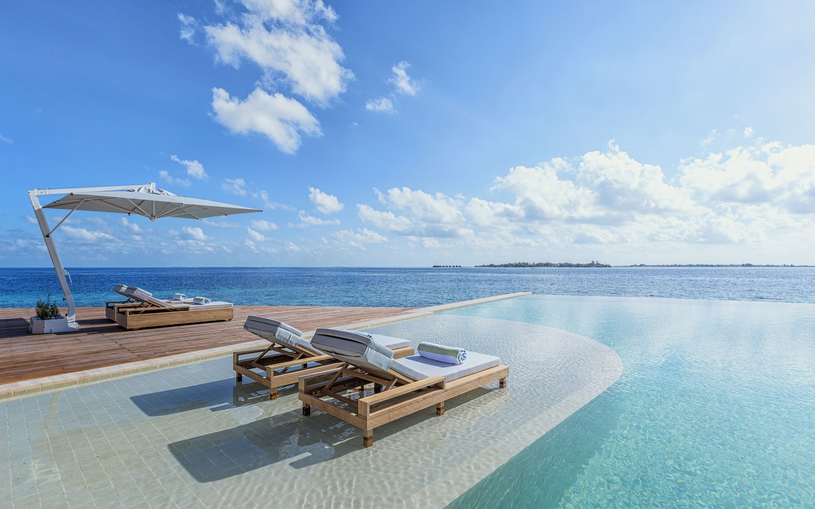 White oval soaking tub on a bathroom platform surrounded by white stones, overlooking turquoise ocean and sky at Kudadoo Maldives Private Island.