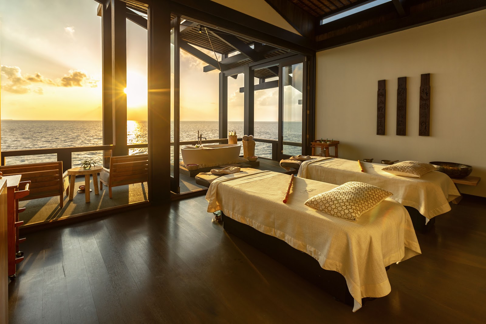 Rope-suspended daybed with cream cushions and throw pillows on a wooden deck under a slatted wooden pergola with ocean views.