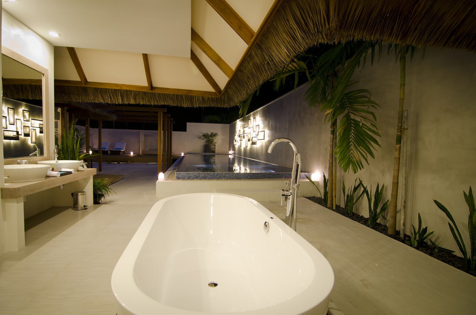 Spacious bathroom at Kuramathi Island Resort with white soaking tub, double vanity, and thatched ceiling overlooking ocean and infinity pool.
