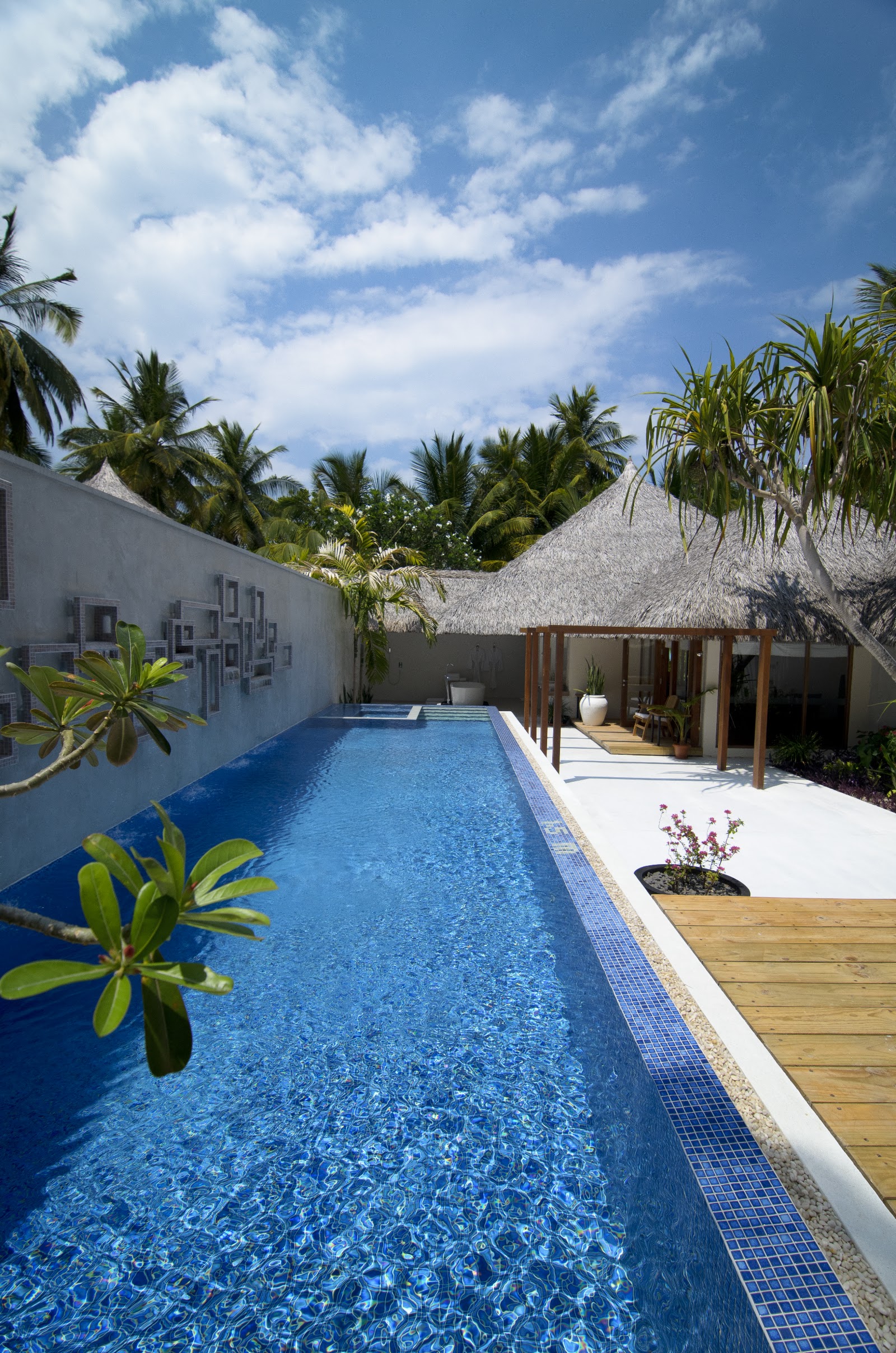 Private villa with blue pool, wooden deck, thatched roof bungalow, and palm trees at Kuramathi Island Resort.