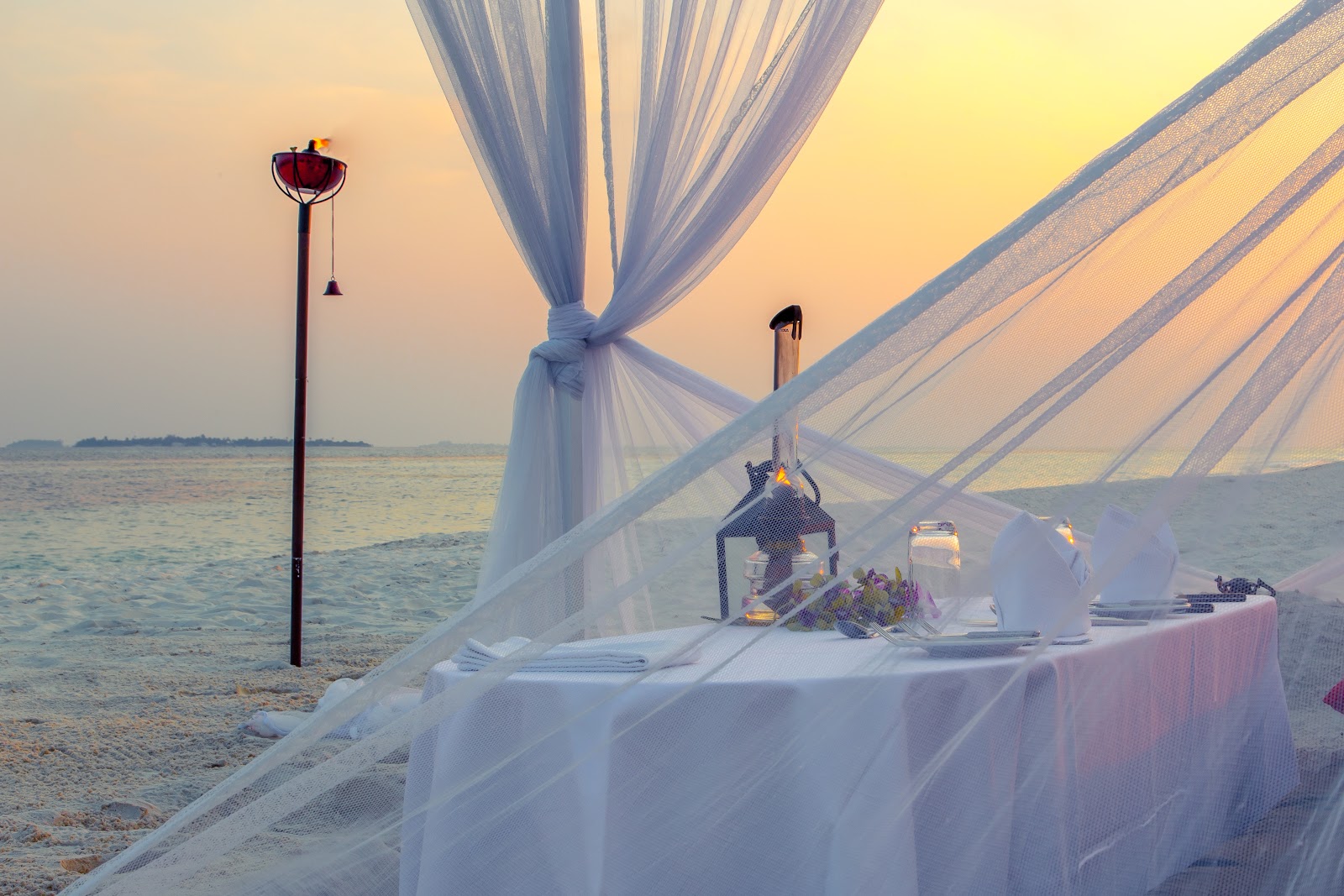 Dining pavilion at Kuredu Island Resort with wooden tables, blue cushioned chairs, and sand floor lit by blue and warm overhead lights.