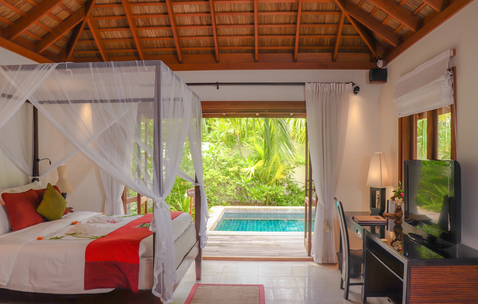 Four-poster bed with sheer white curtains overlooks a private pool through open doors at Kuredu Island Resort & Spa.