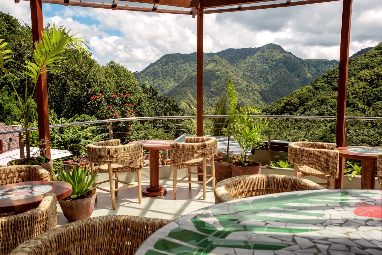 Covered terrace with woven chairs and wooden tables overlooks lush green mountains under a wooden pergola at Ladera Resort.