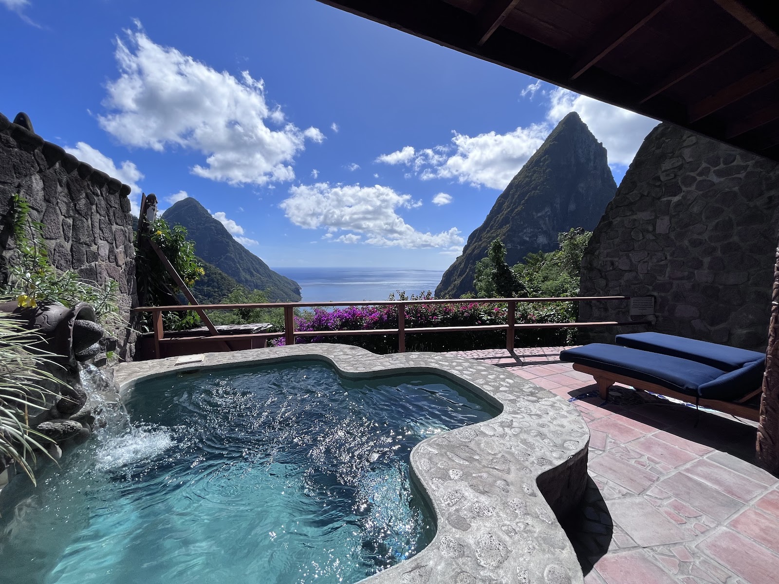 Wooden swing suspended over turquoise pool water with dramatic piton rock formation and sun glare in background at Ladera Resort.