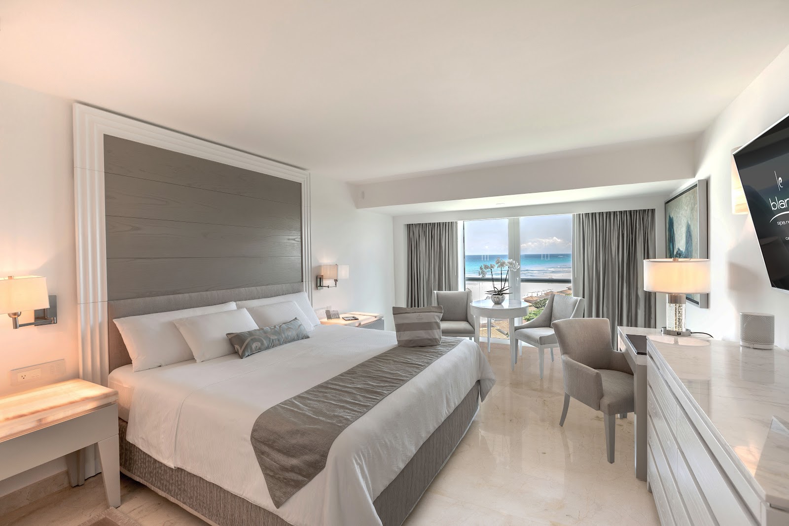 Resort guest room with king bed, seating area, and ocean view through floor-to-ceiling windows at Le Blanc Spa Resort Cancun.
