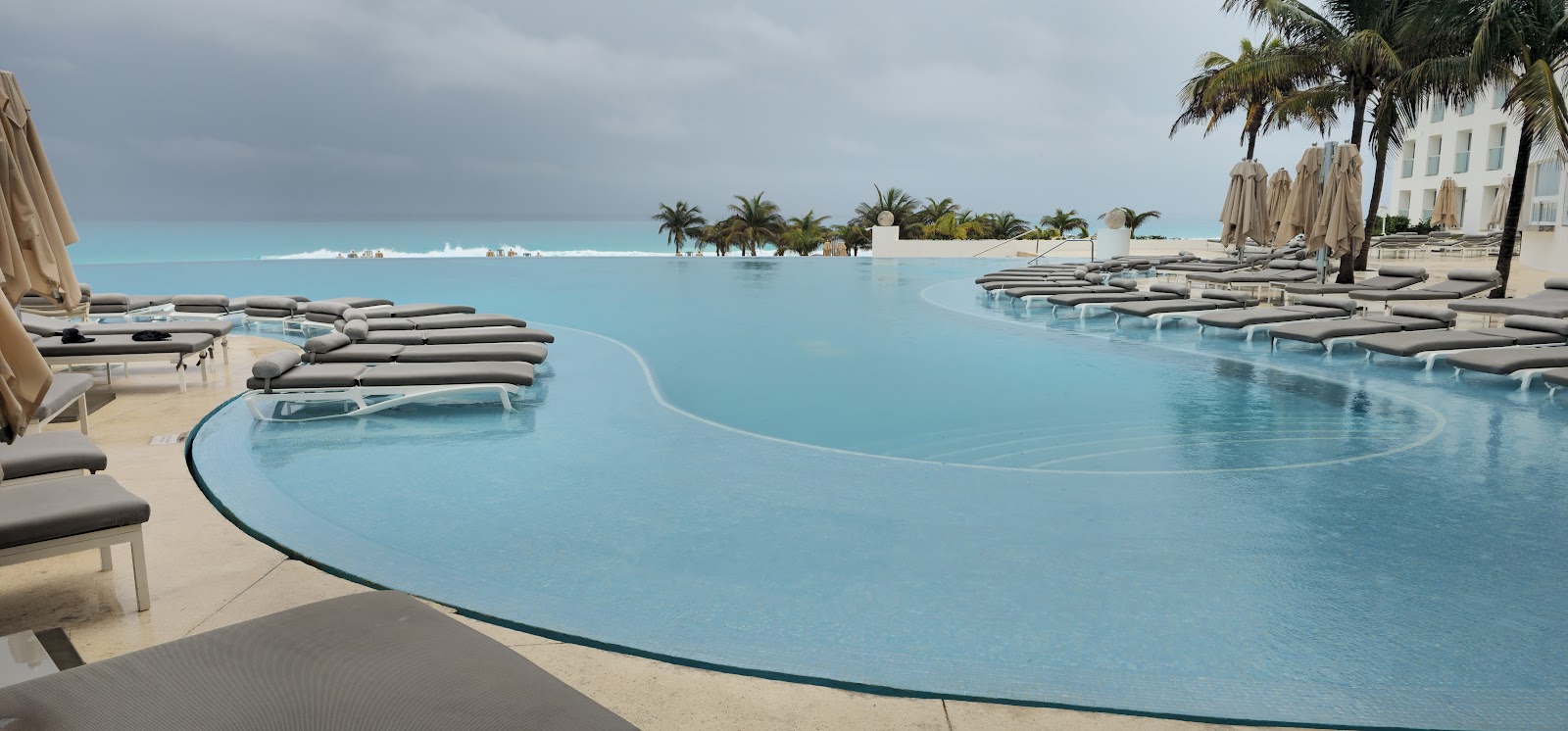 Curved infinity pool with turquoise water, lounge chairs, and palm trees at Le Blanc Spa Resort Cancun.