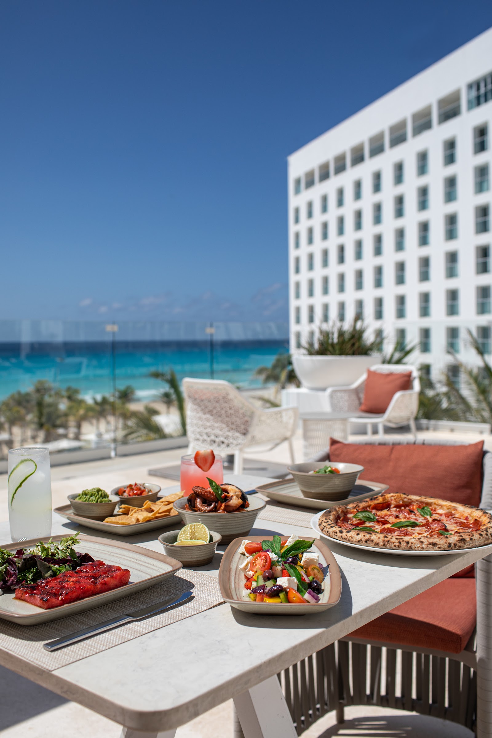 Beachfront dining table at Le Blanc Spa Resort Cancun with pizza, seafood, and salads overlooking turquoise Caribbean waters.
