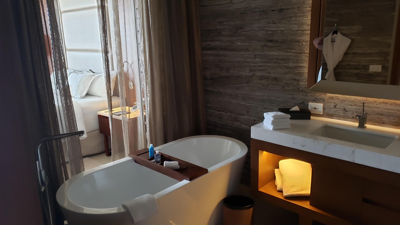 Spa bathroom with two soaking tubs, dark wood accents, white marble countertop sink, and illuminated shelving holding yellow towels.