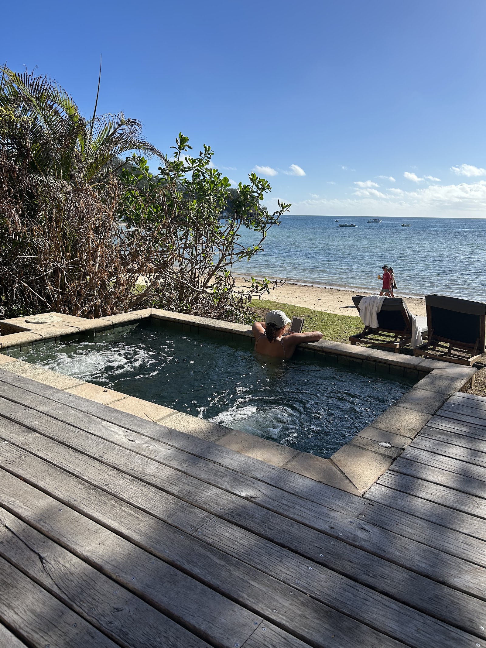 Pool with loungers and umbrellas flows into turquoise ocean, framed by palm trees and distant islands under clear blue sky at Likuliku Lagoon Resort.