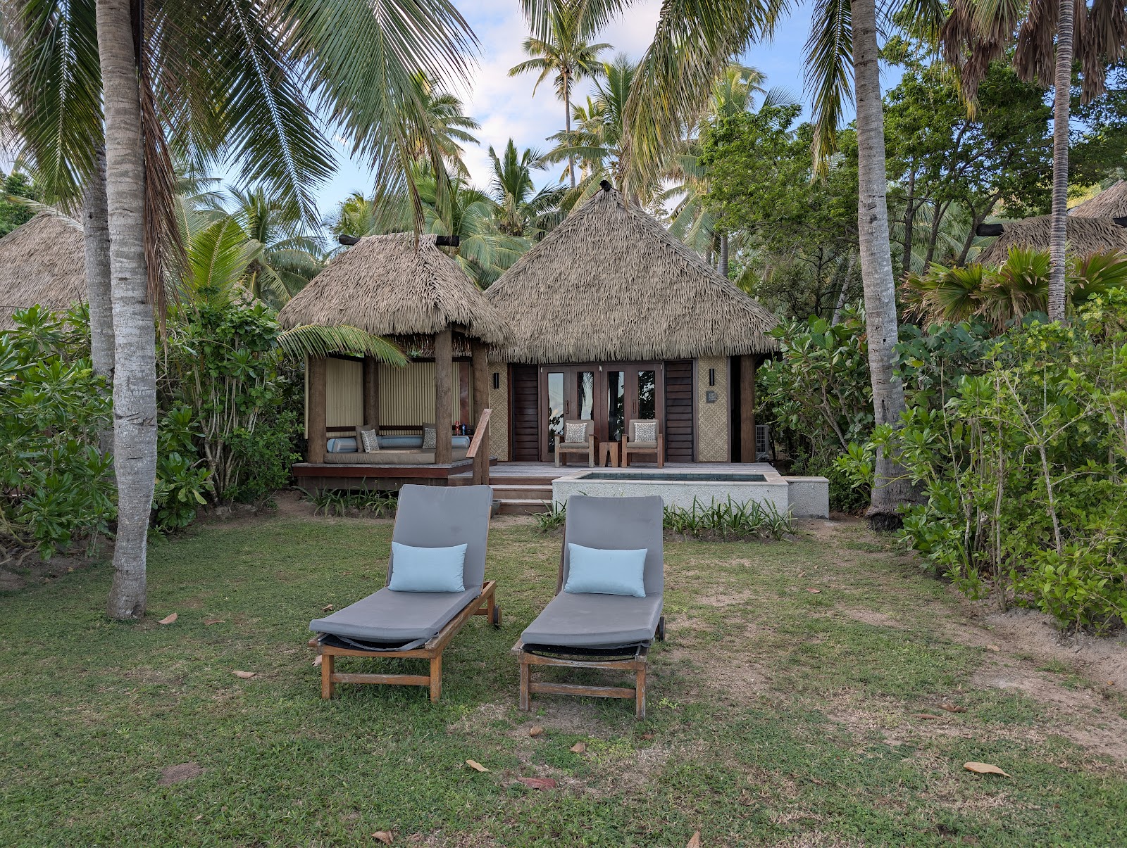 Beachfront dining area at Likuliku Lagoon Resort with palm trees, sandy beach, and turquoise lagoon water under clear sky.