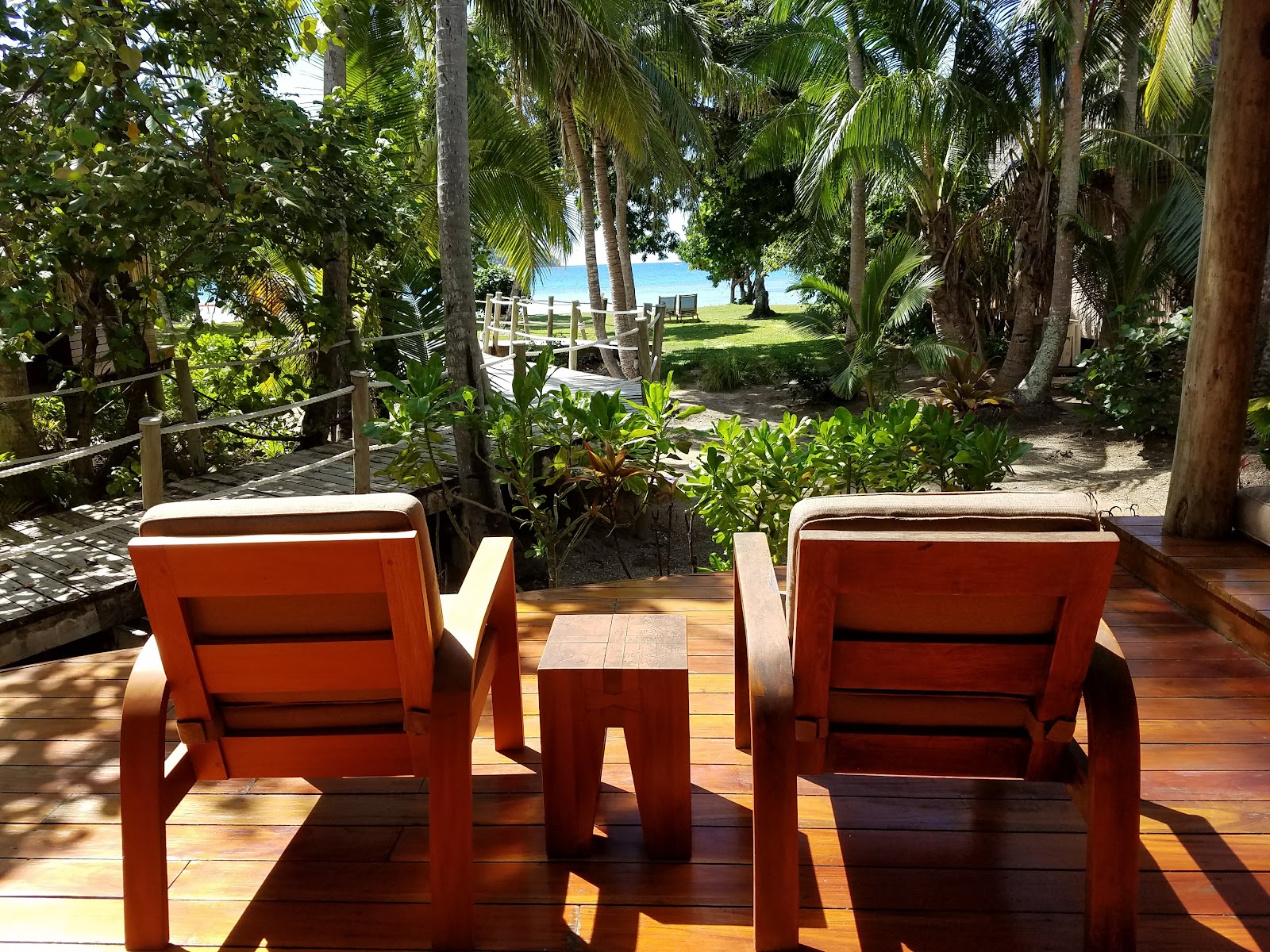 Resort bedroom with king bed decorated with welcome message, tropical flowers, and traditional Fijian sandals, flanked by dark wood nightstands with lamps.