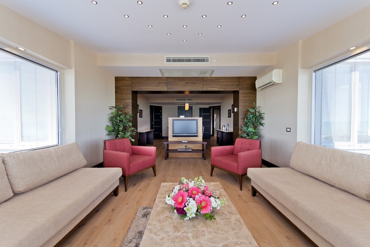 Spacious suite living room with beige sofas, pink armchairs, flat-screen TV, and pink flower arrangement at Limak Lara De Luxe Hotel & Resort.