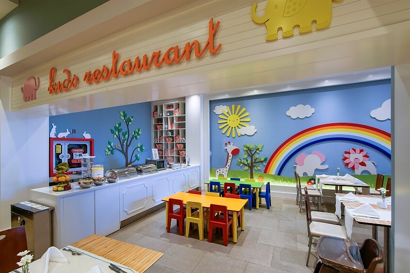 Kids restaurant with colorful rainbow mural, serving counter, and child-sized tables and chairs at Limak Lara De Luxe Hotel & Resort.
