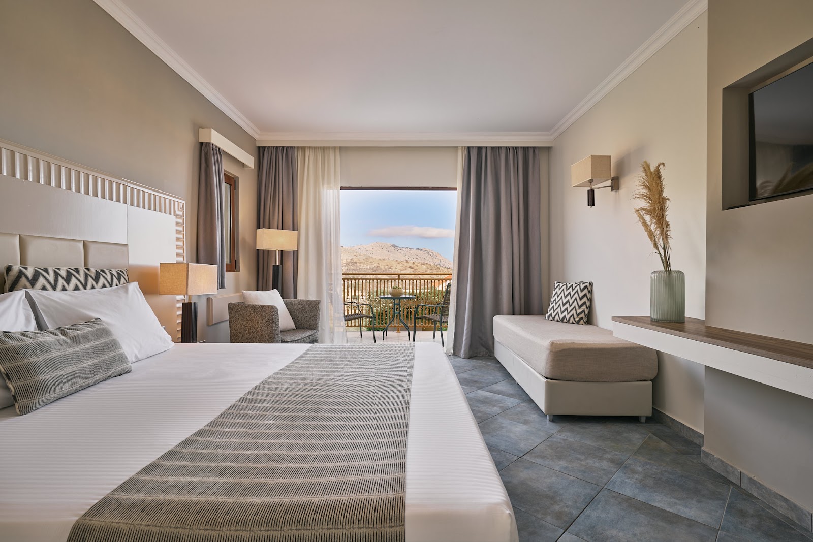 Hotel room at Lindos Imperial Resort & Spa with bed, balcony seating, and view of desert mountains beyond the terrace.