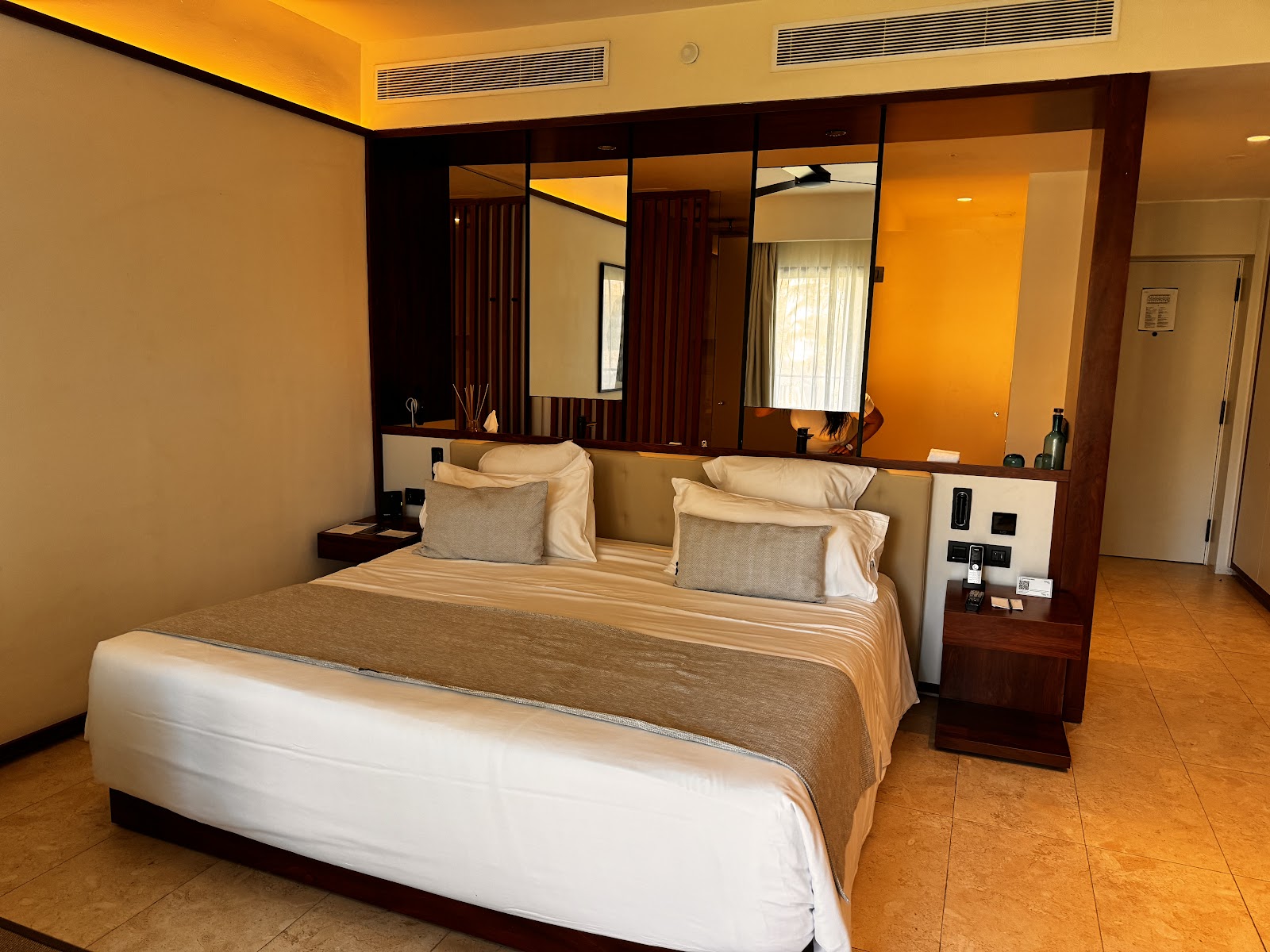 Resort bedroom with queen bed, large mirror vanity, dark wood accents, and terracotta tile flooring at Live Aqua Beach Resort Punta Cana.