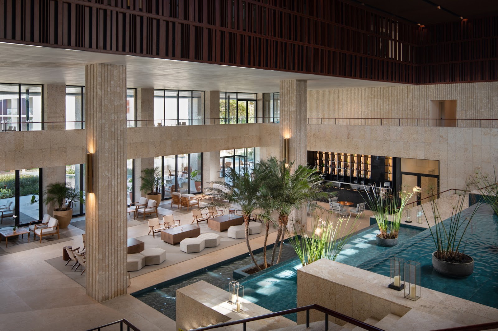 Indoor pool at Live Aqua Beach Resort Punta Cana surrounded by lounge seating, potted plants, and a crystal chandelier overhead.