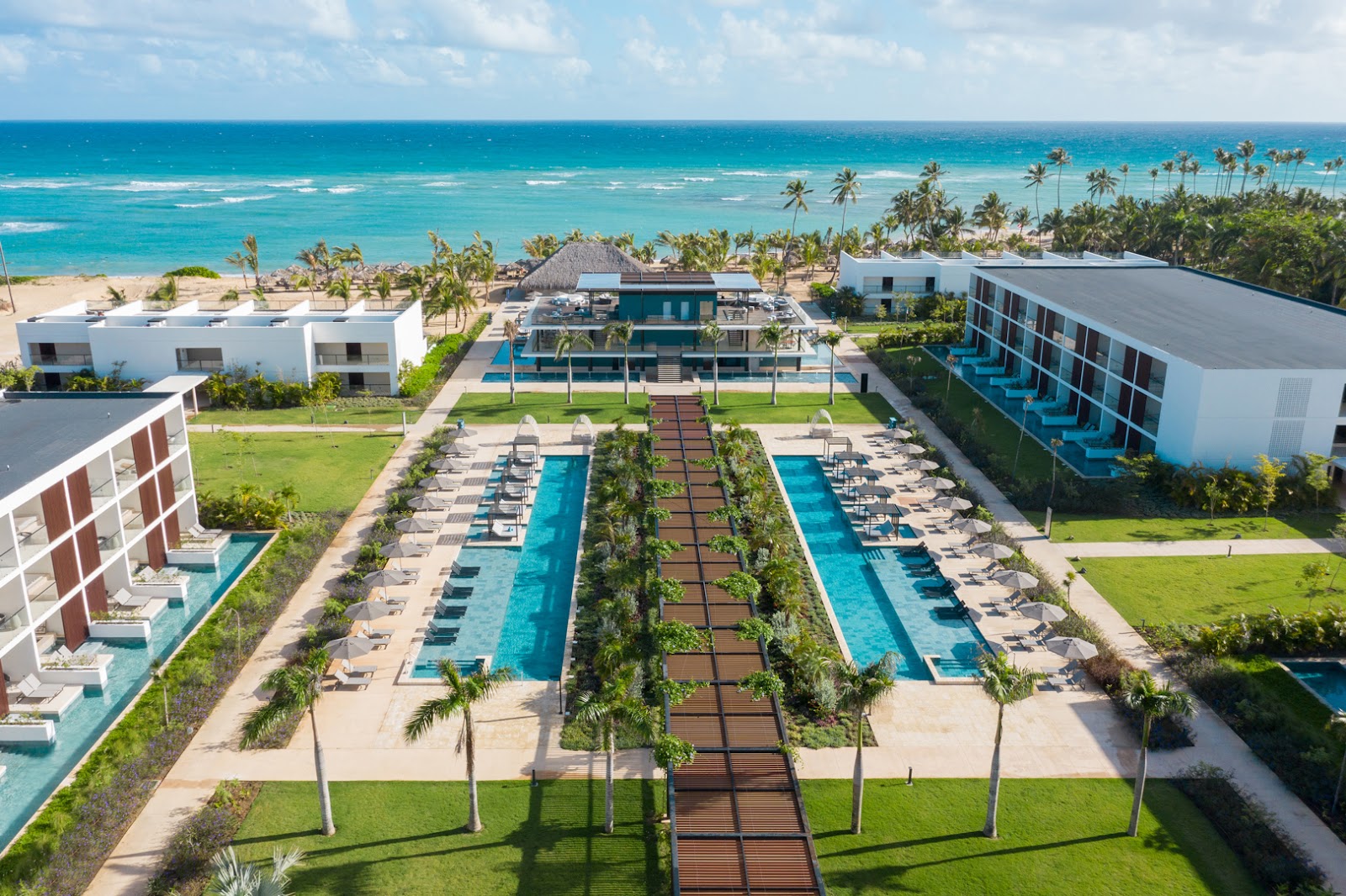 Modern lobby with indoor pool, potted palms, cream seating areas, and tall fluted columns at Live Aqua Beach Resort Punta Cana.