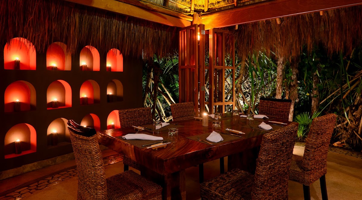 Candlelit dining room at Live Aqua Beach Resort Cancún with glowing red alcove wall, woven chairs, and tropical plants.