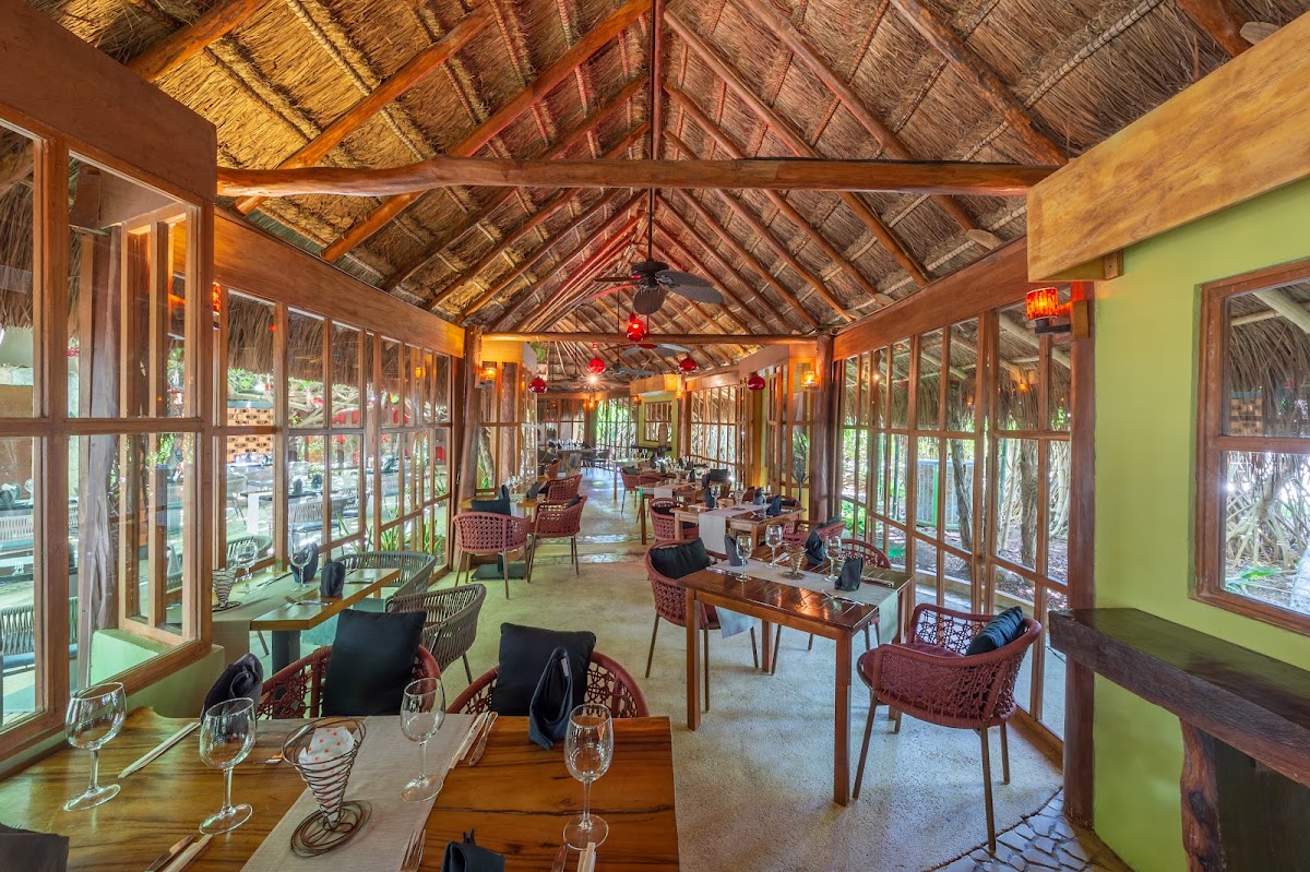 Dining room with wooden tables, woven thatch ceiling, and floor-to-ceiling windows overlooking tropical grounds at Live Aqua Beach Resort Cancún.