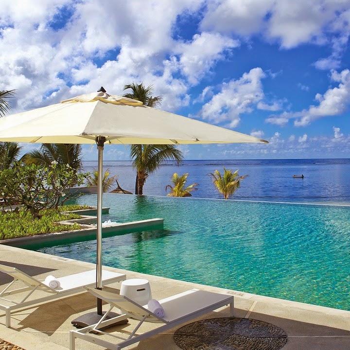 Cream umbrella and lounge chairs on a sandy deck overlooking a turquoise infinity pool and calm ocean at Long Beach Mauritius.