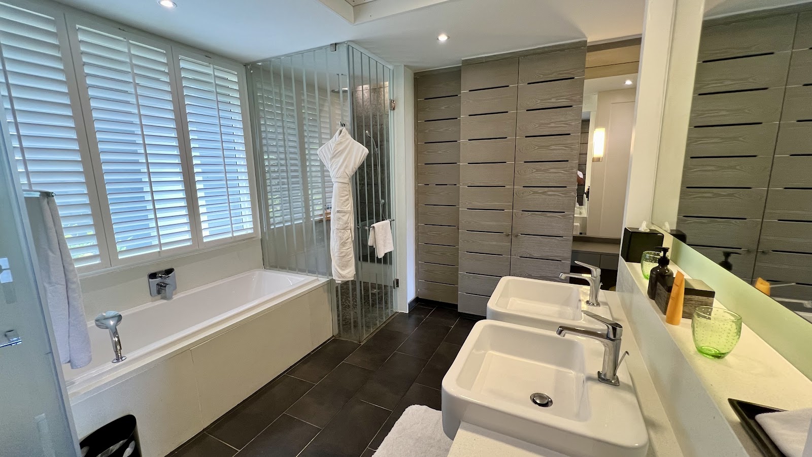 Bathroom with double sinks, soaking tub with glass enclosure, and dark tile flooring at Long Beach Mauritius.