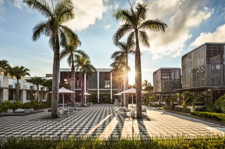 Tiled courtyard at Long Beach Mauritius with tall palm trees, modern buildings, and white umbrellas under afternoon sun.