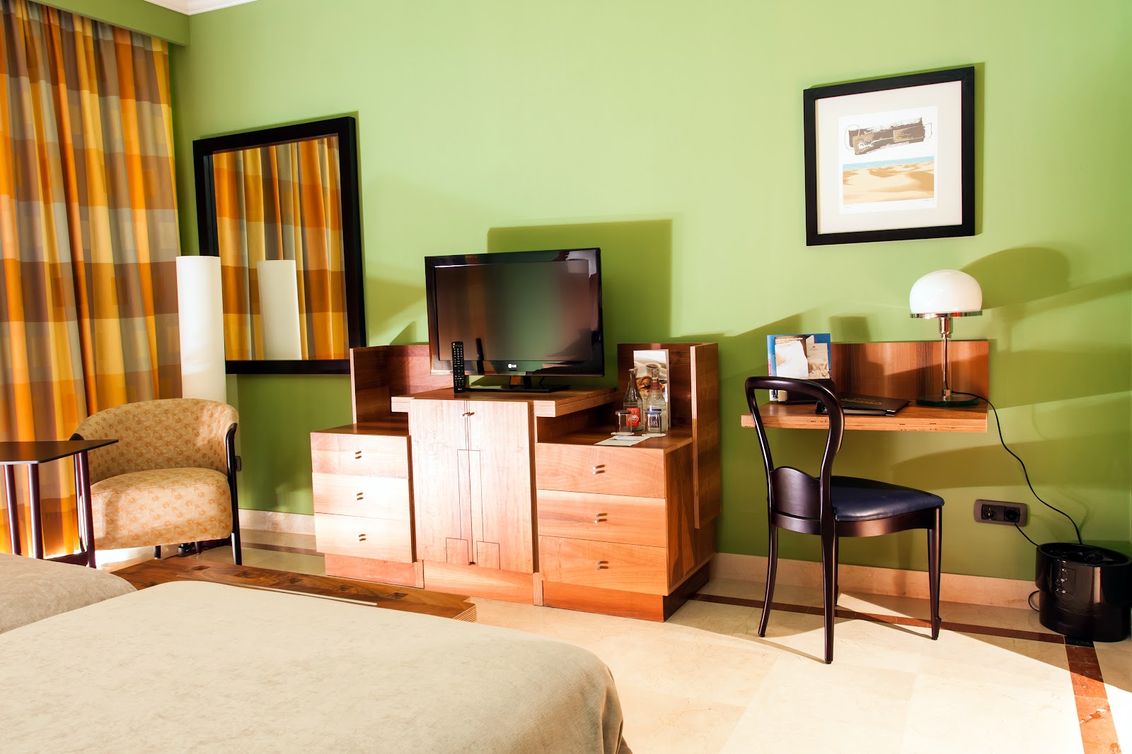 Bright green resort bedroom with wooden furniture, TV, desk chair, striped orange curtains, and framed artwork on walls.