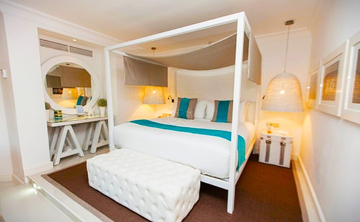 White canopy bed with teal accents and vanity mirror in a bright bedroom at LUX* Belle Mare.