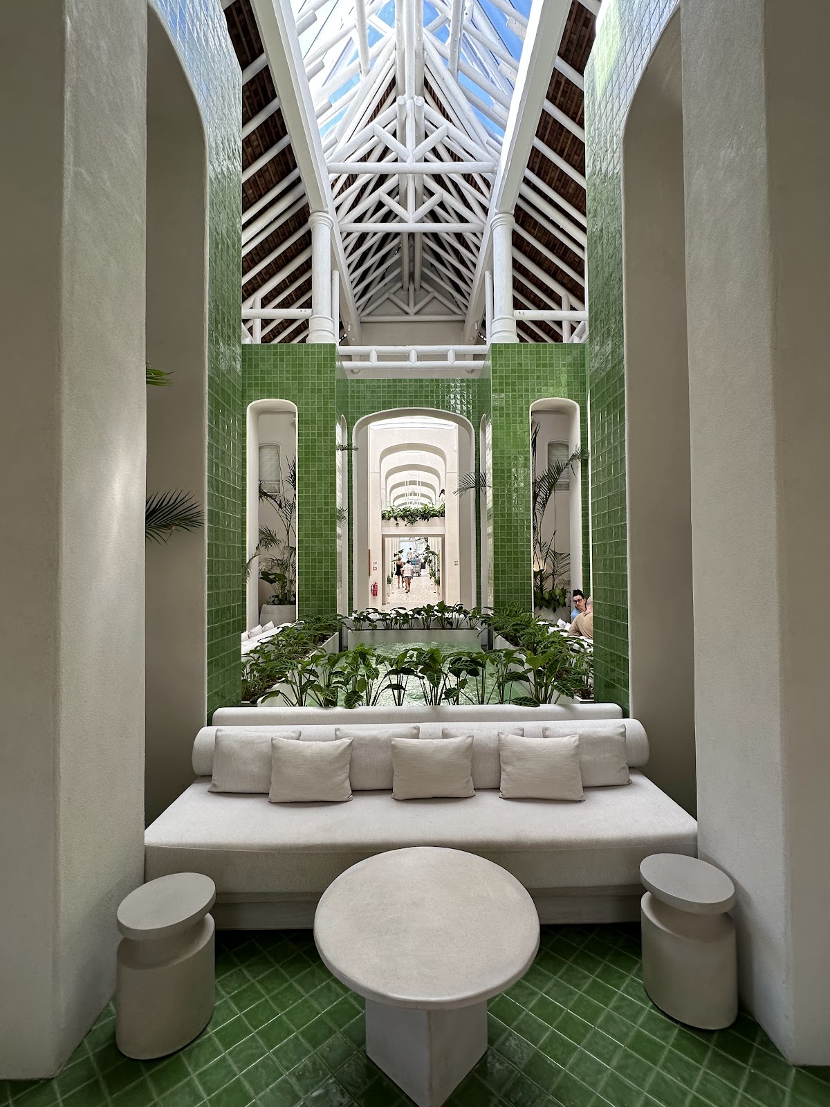 Green tiled courtyard with white bench seating, potted plants, and geometric skylights overhead at LUX* Belle Mare.
