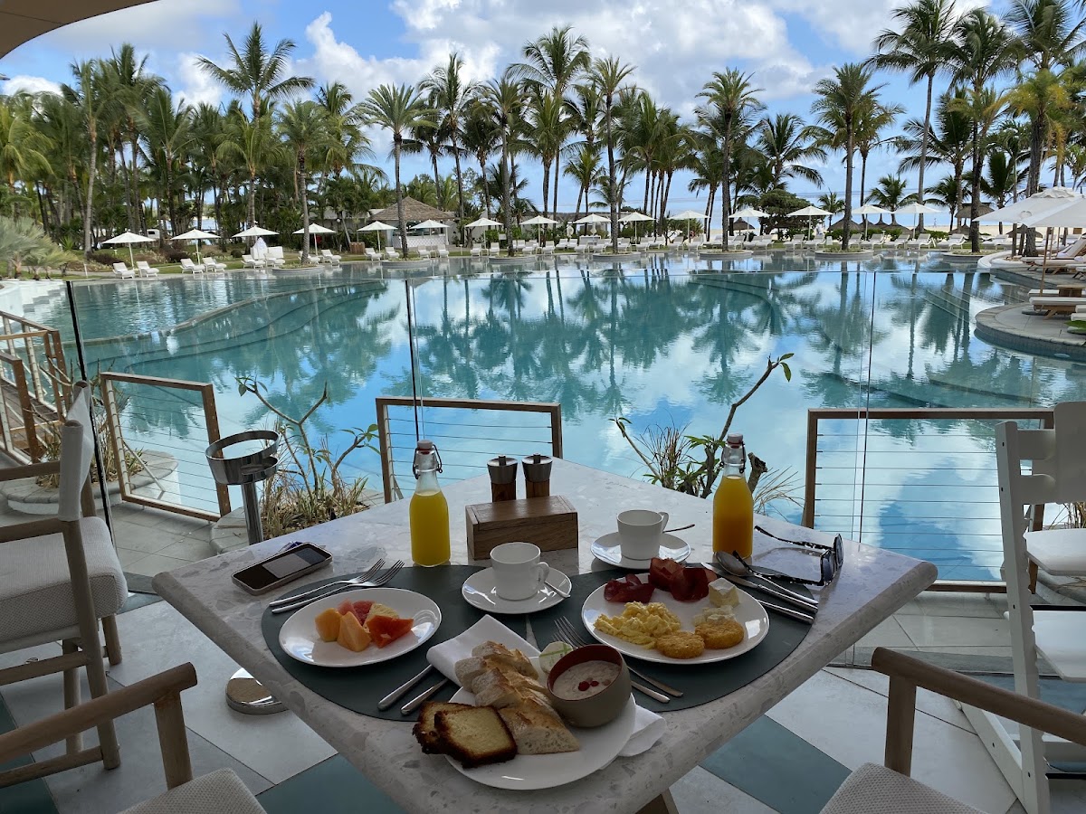 Breakfast table set with fruit, pastries, and juice overlooking the pool and palm trees at LUX* Belle Mare.