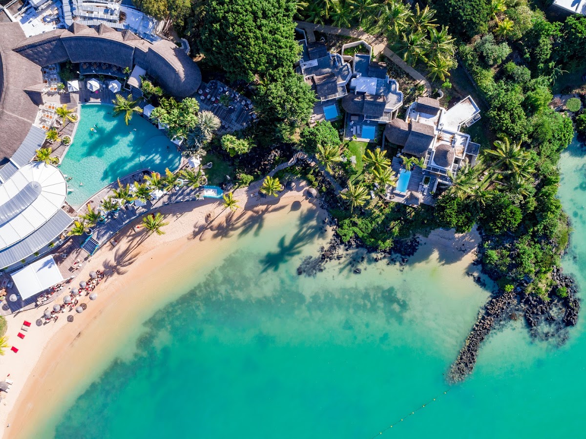 Aerial view of LUX Grand Gaube's curved pool and sandy beach surrounded by lush tropical vegetation and turquoise lagoon waters.