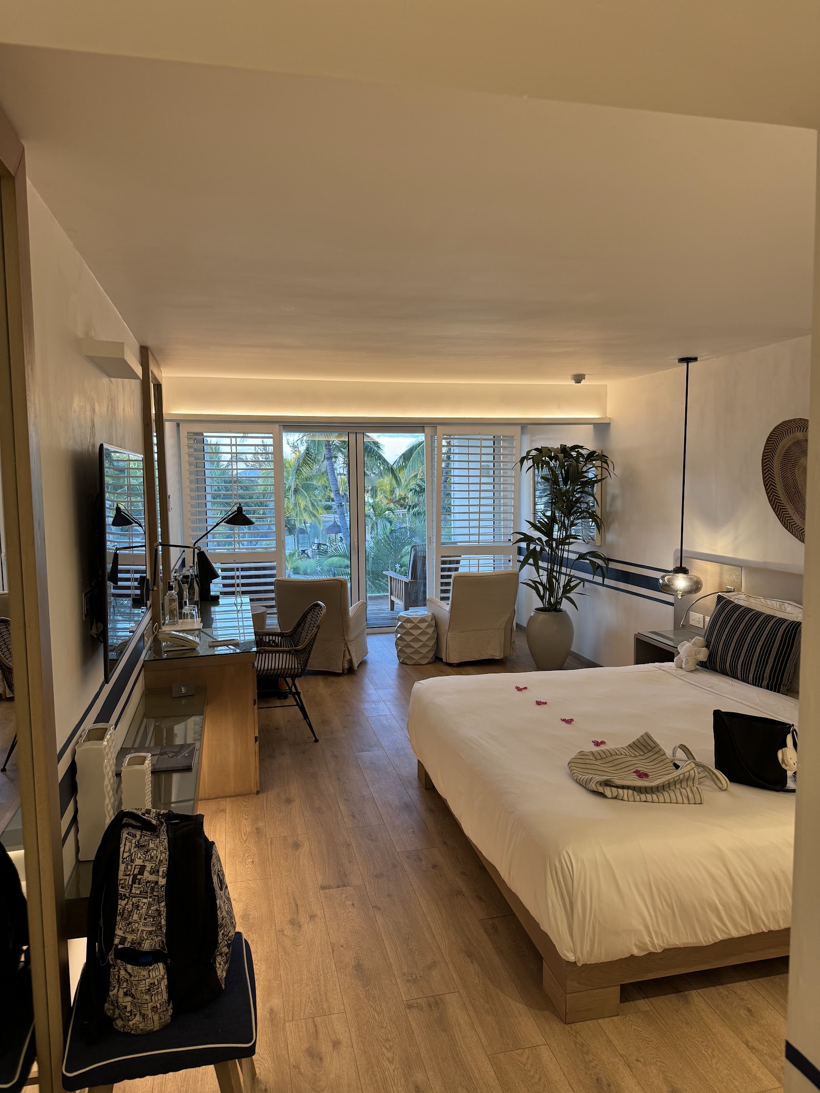 Spacious resort suite with king bed, sitting area, and oceanview balcony with palm trees visible through shuttered doors.