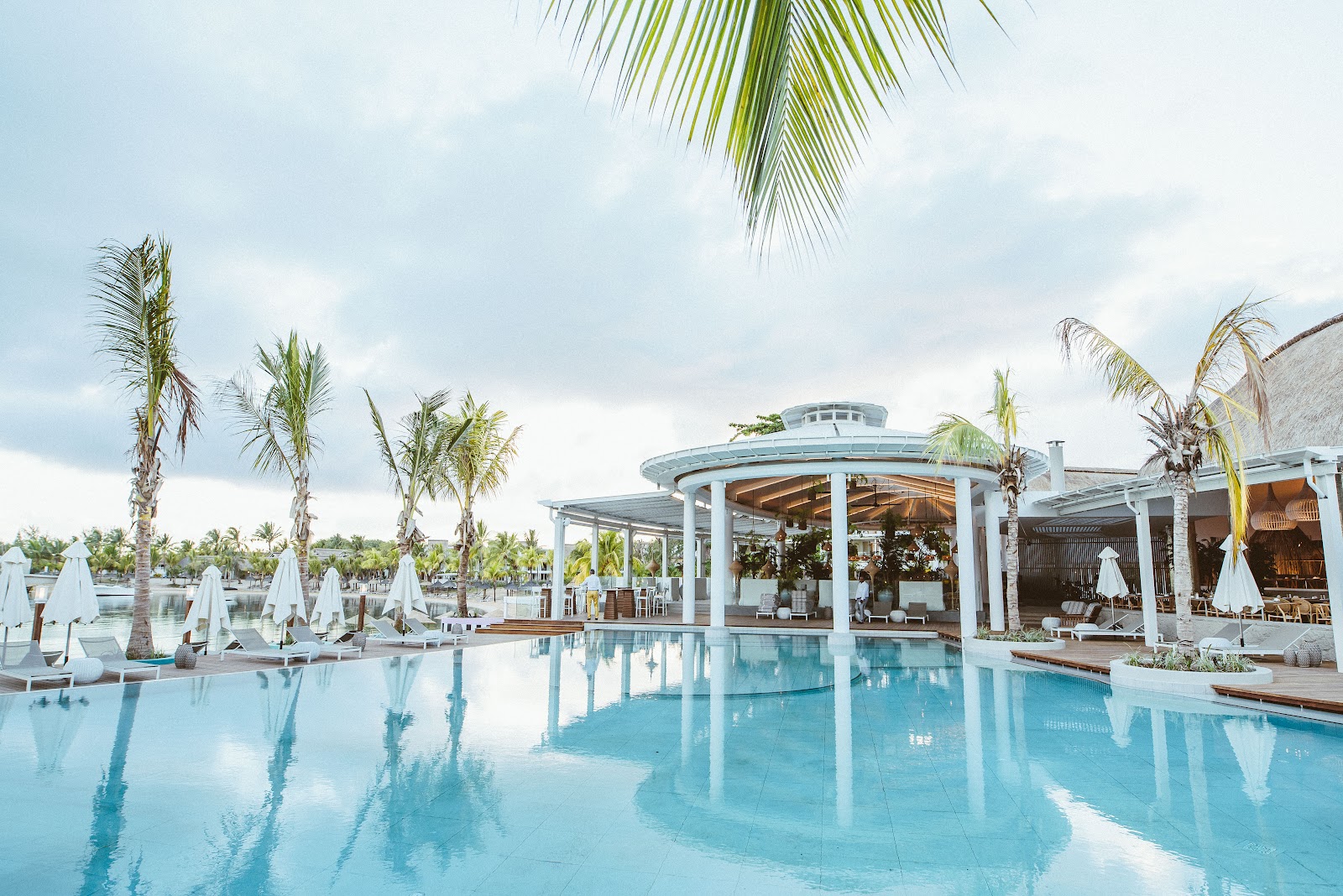 Turquoise pool with white umbrellas and loungers alongside a circular gazebo-style pavilion with columns at LUX Grand Gaube.