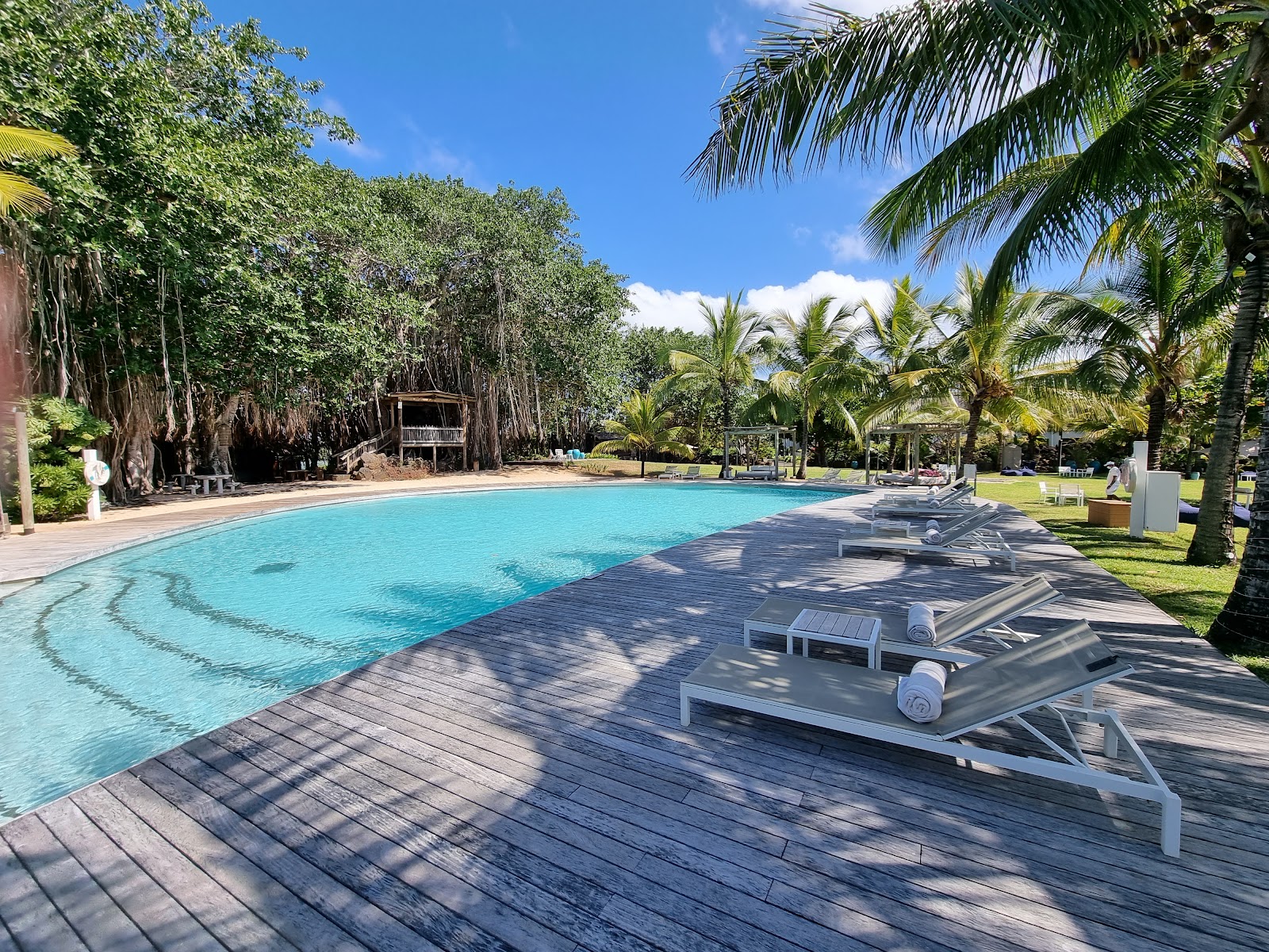 Aerial view of LUX Grand Gaube showing beachfront resort with curved pool, palm trees, and turquoise lagoon waters with distant island.