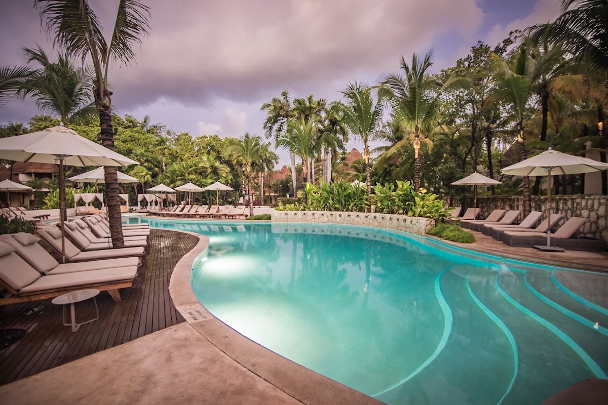 Curved lagoon-style pool with turquoise water surrounded by lounge chairs, umbrellas, and palm trees at Mahekal Beach Resort.